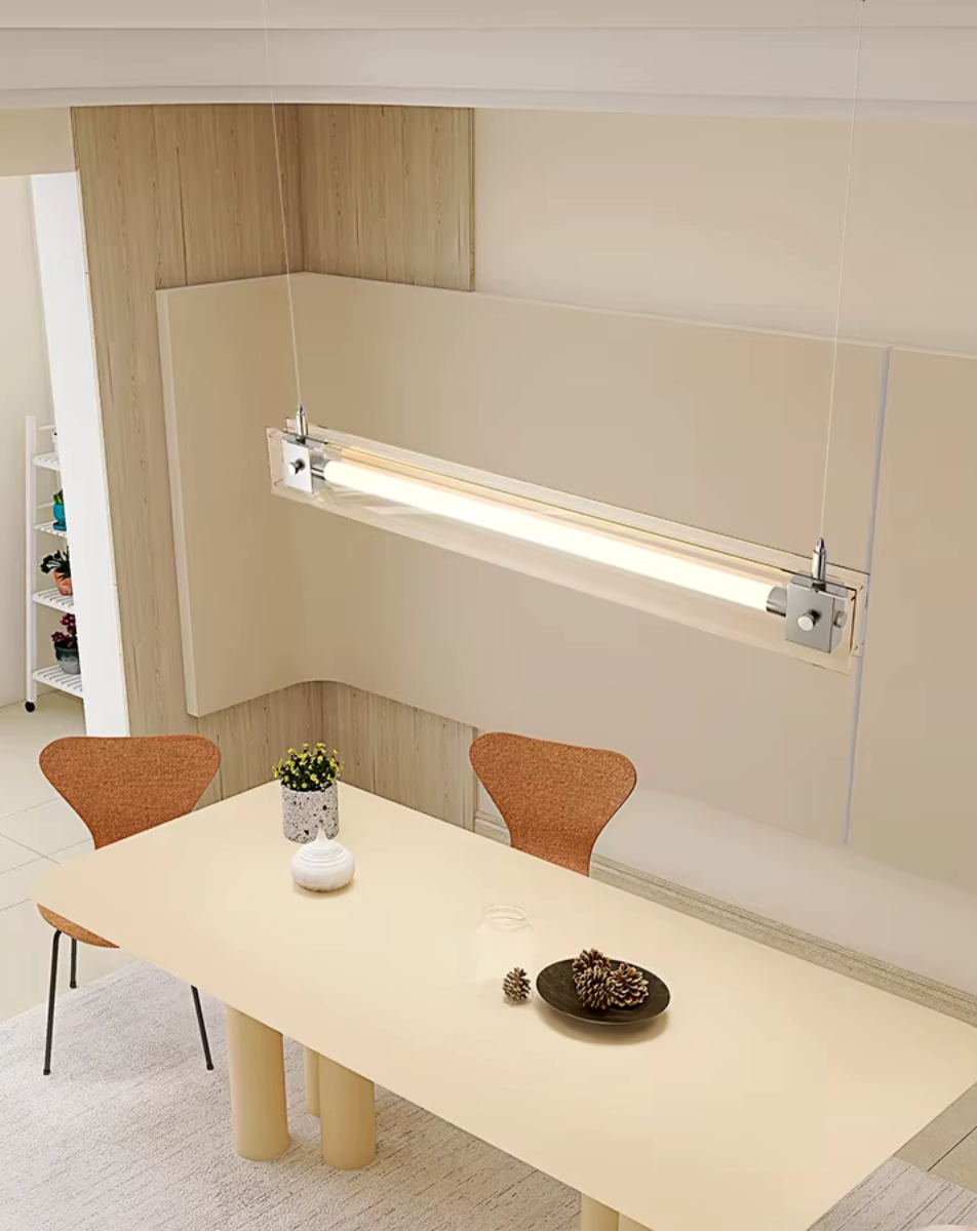 A modern, sleek linear glass pendant light with stainless steel accents, suspended over a counter, dispersing a warm glow.