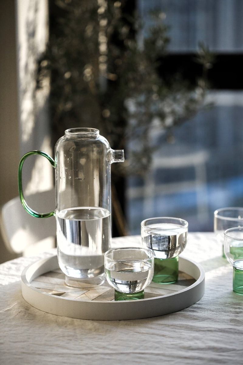 tall round clear glass pitcher with green handle and cup with green base