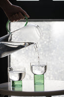 tall round clear glass pitcher with green handle and cup with green base