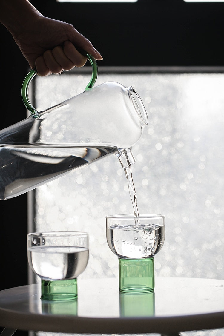 tall round clear glass pitcher with green handle and cup with green base