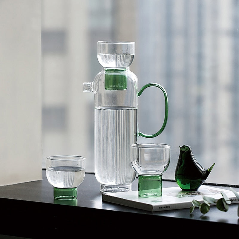 tall round clear glass pitcher with green handle and cup with green base